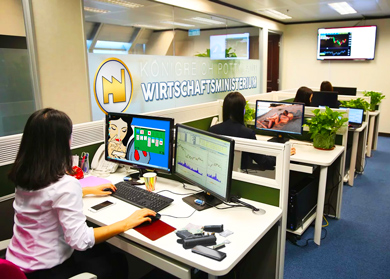 Im Wirtschaftsministerium wird sich stets bemüht, fleißig arbeitend zu wirken. Ein mittleres Büro mit Menschen, Schreibtischen, Computern und lustigen Bildschirmhintergründen